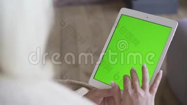 一个拿着绿色屏幕的白色平板电脑的女人的手。 女人坐着看着平板电脑。 使用小玩意的金发女人